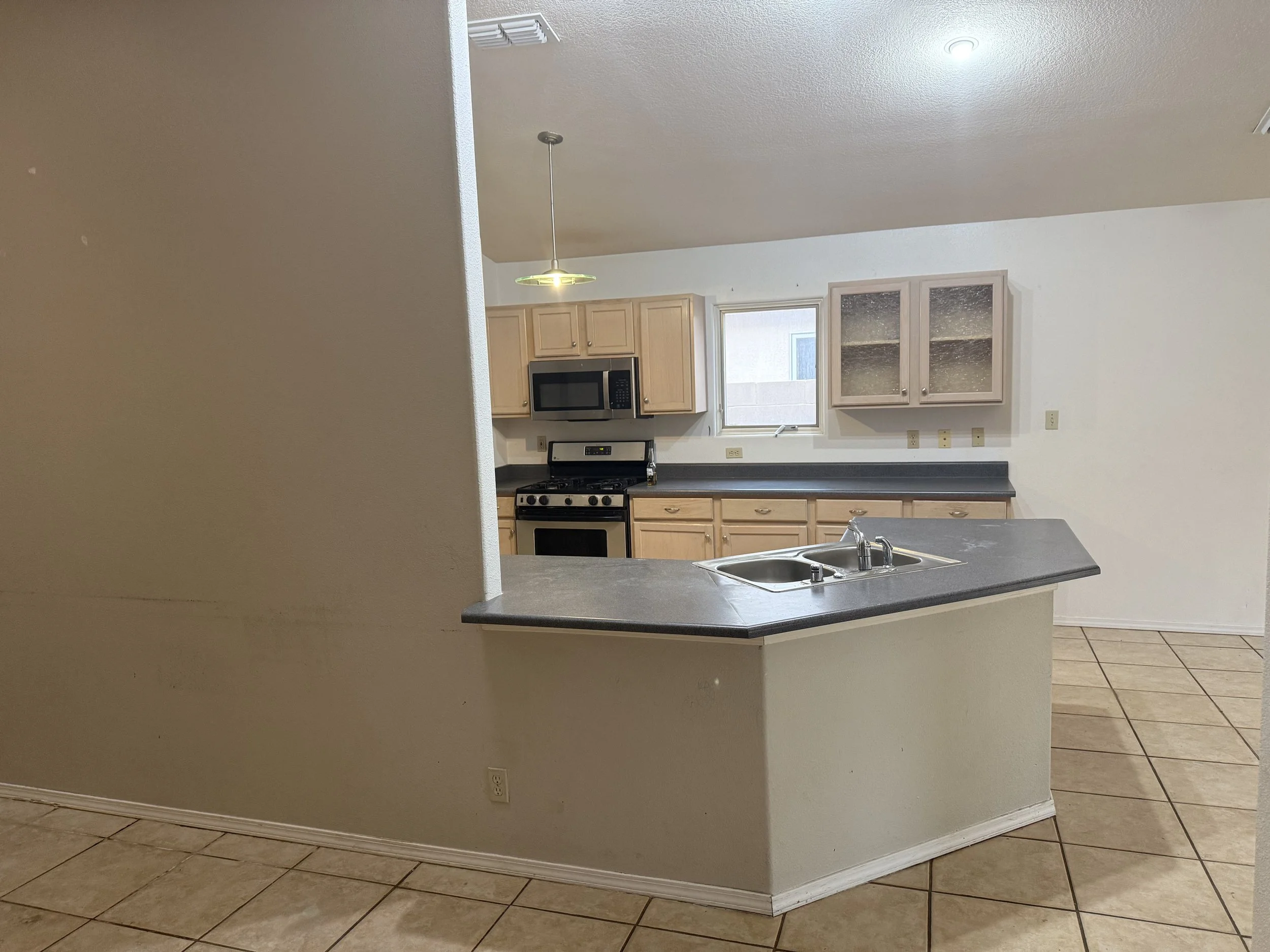 Interior view of a kitchen with wooden cabinets, a black stove, microwave, a window, and a kitchen island with a sink, seen from a partial wall.