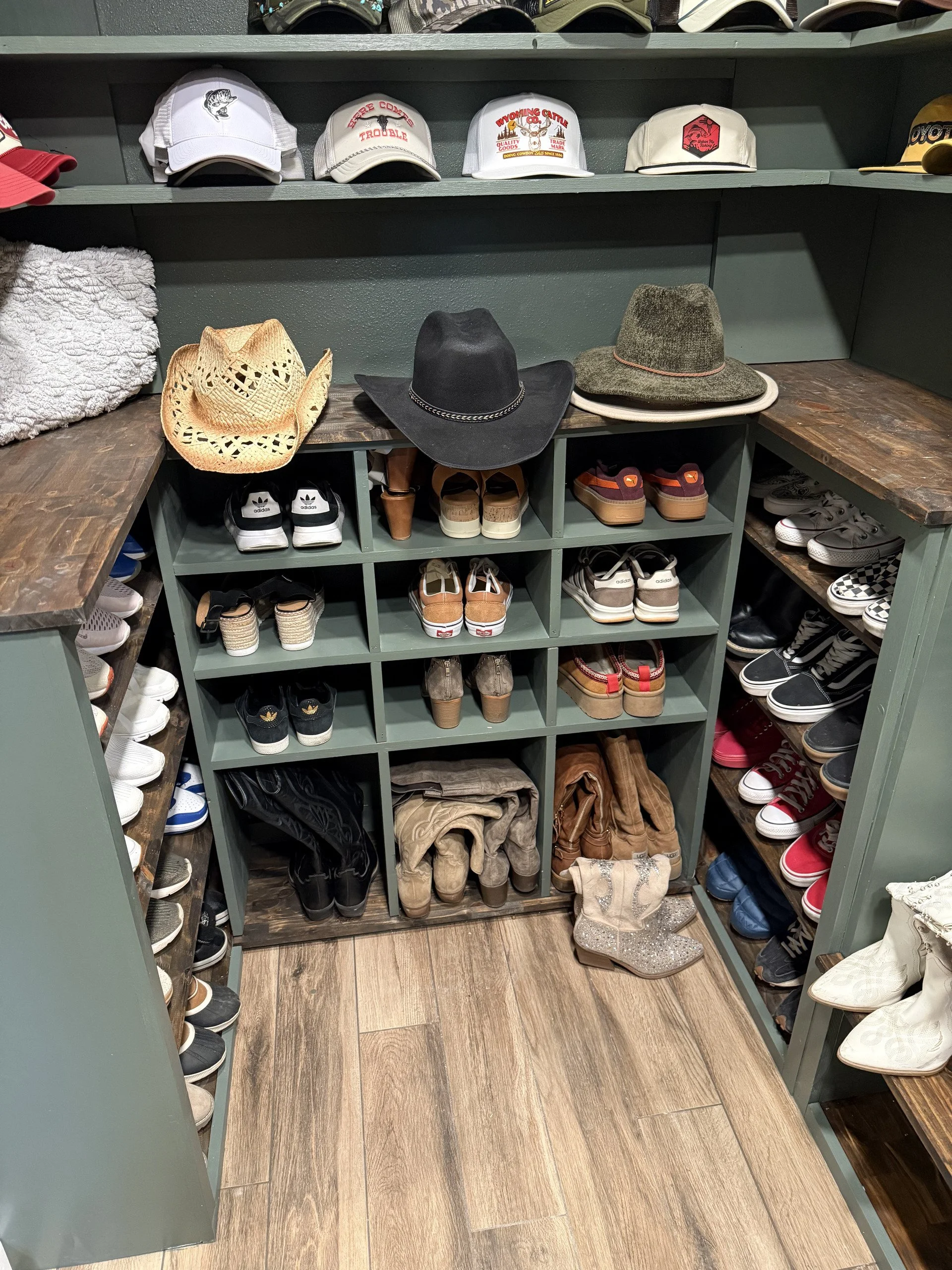 Finished closet with various hats on shelves including baseball caps and cowboy hats, along with row of shoes and boots on shelves below.