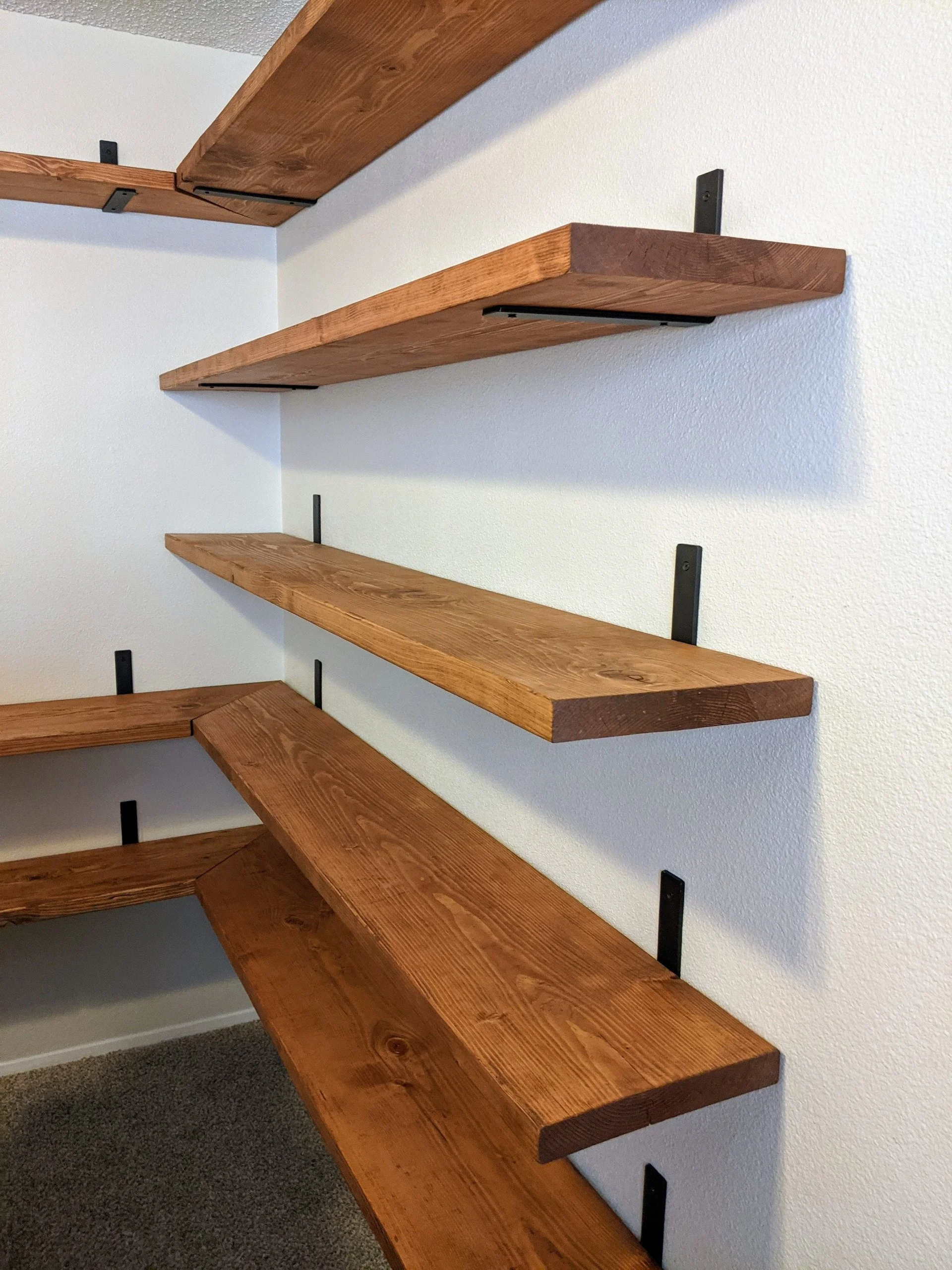 Three wooden shelves mounted on a white wall, supported by black brackets.