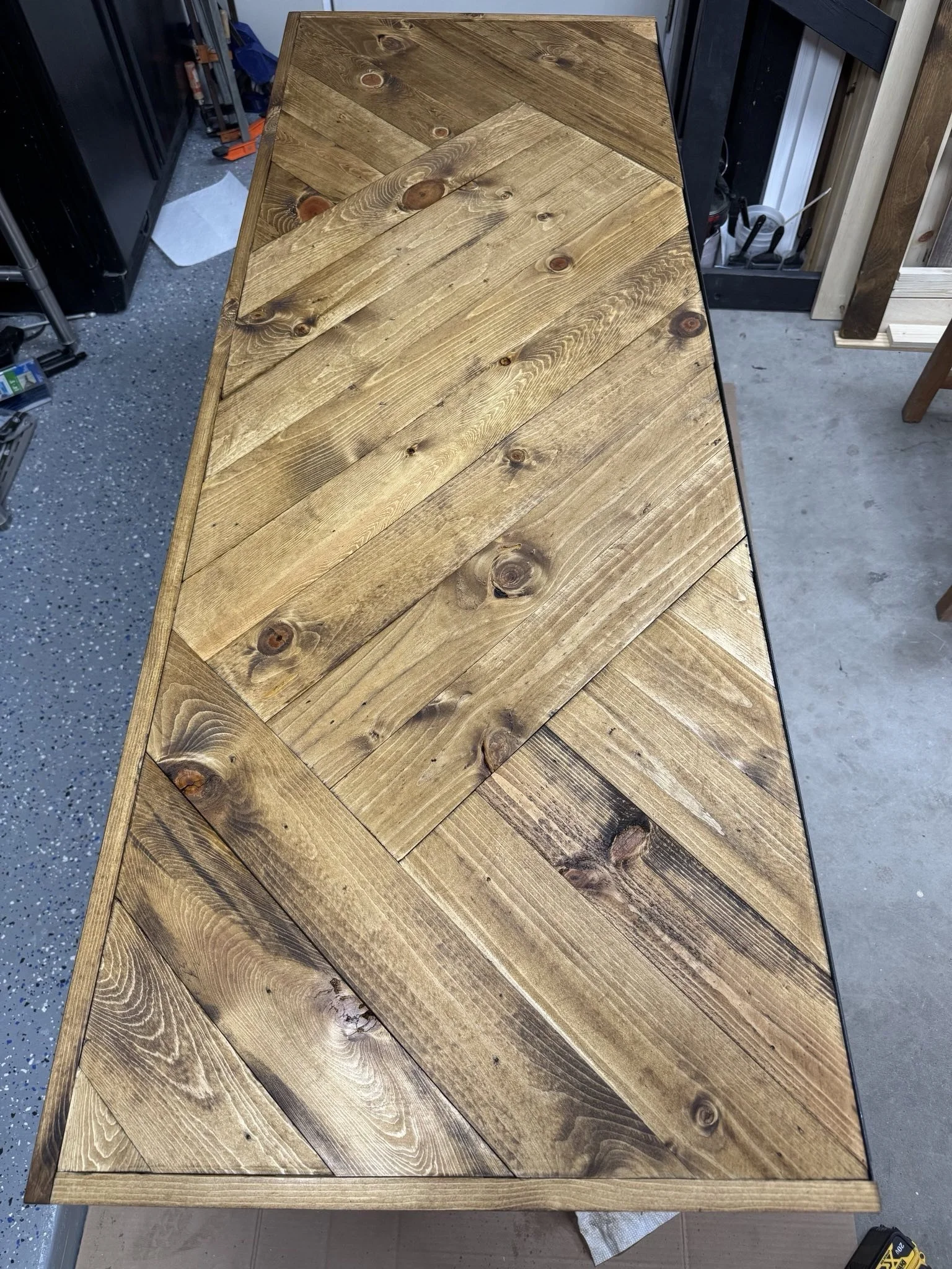 A wooden table with a chevron pattern on top in a workshop or garage setting.
