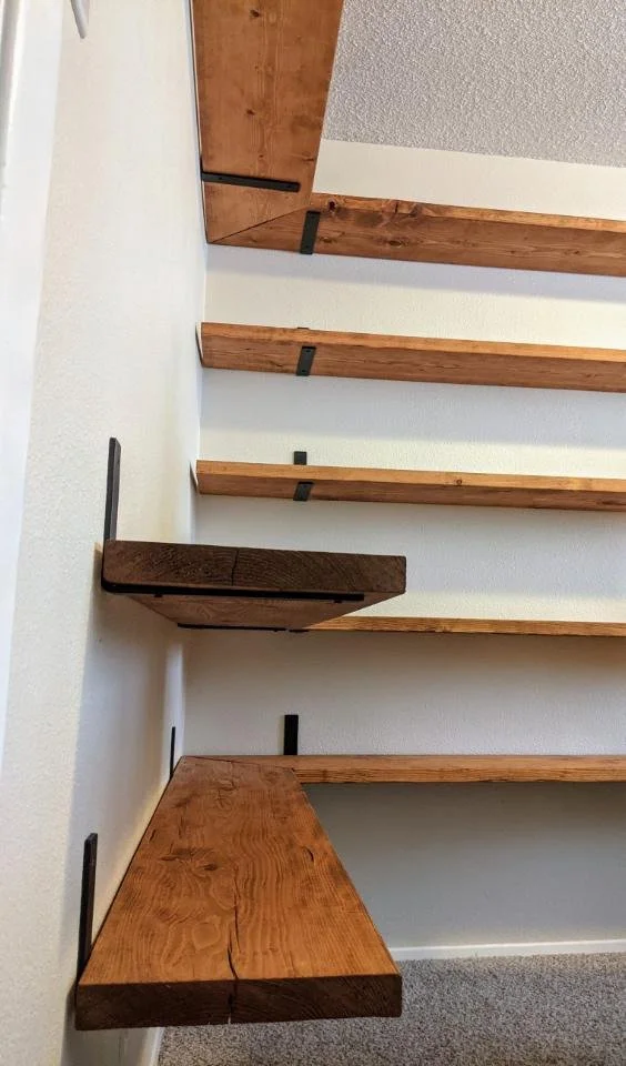 Empty wooden wall shelves of various sizes mounted on a white wall with black brackets.