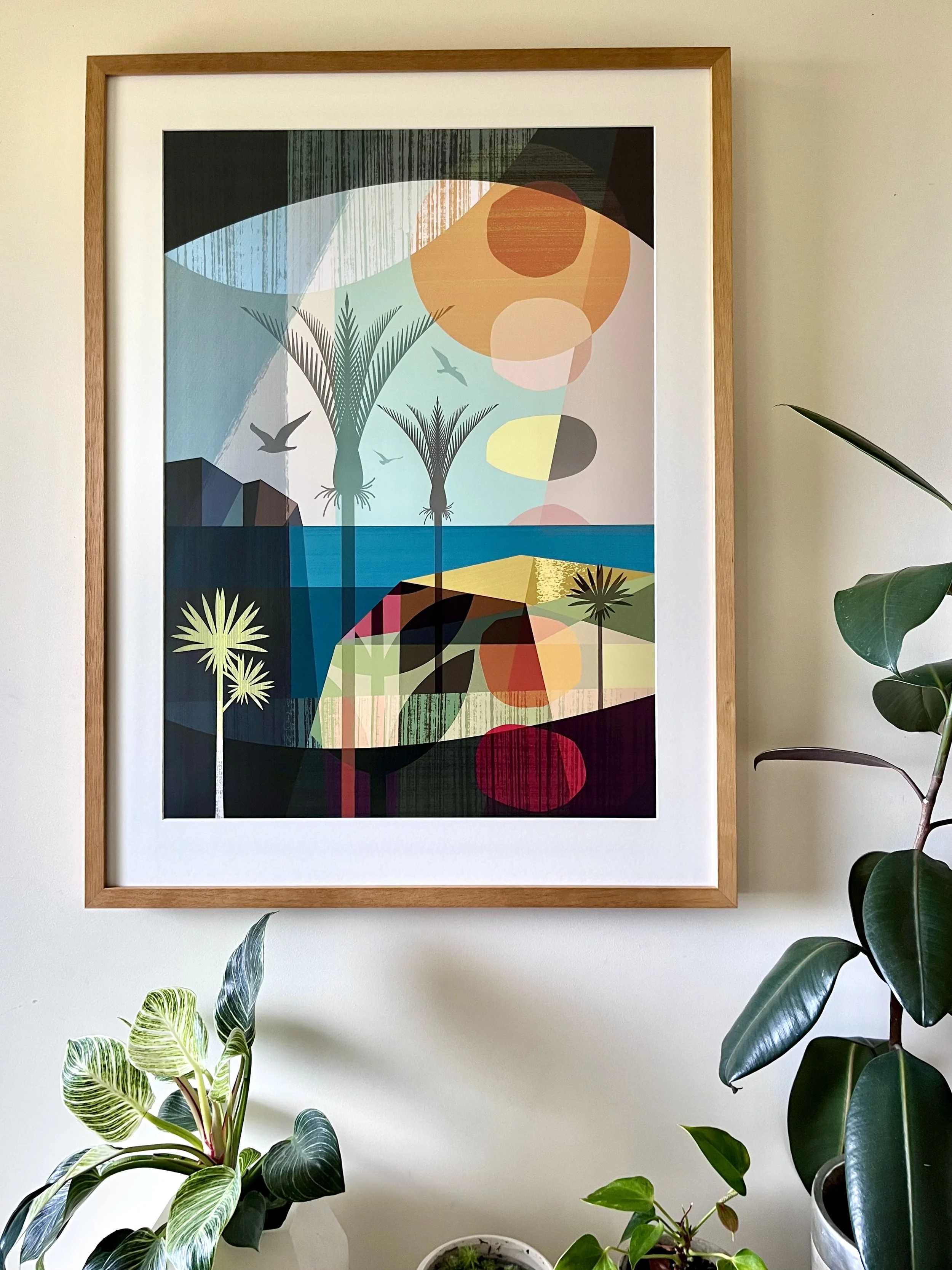 A colorful abstract framed artwork by Ellen Giggenbach hanging on a white wall, surrounded by green houseplants.