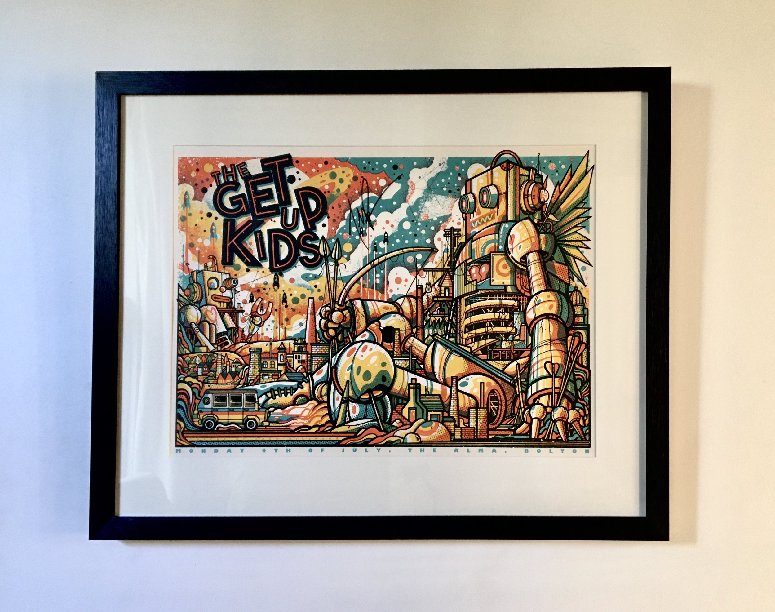 Framed colorful illustration by Drew Millward From the "The Get Up Kids" gig at the Alma Inn, Bolton. Showing illustrations of buildings, giant robots, radio towers, and a parade with a bus, fireworks, and flags.