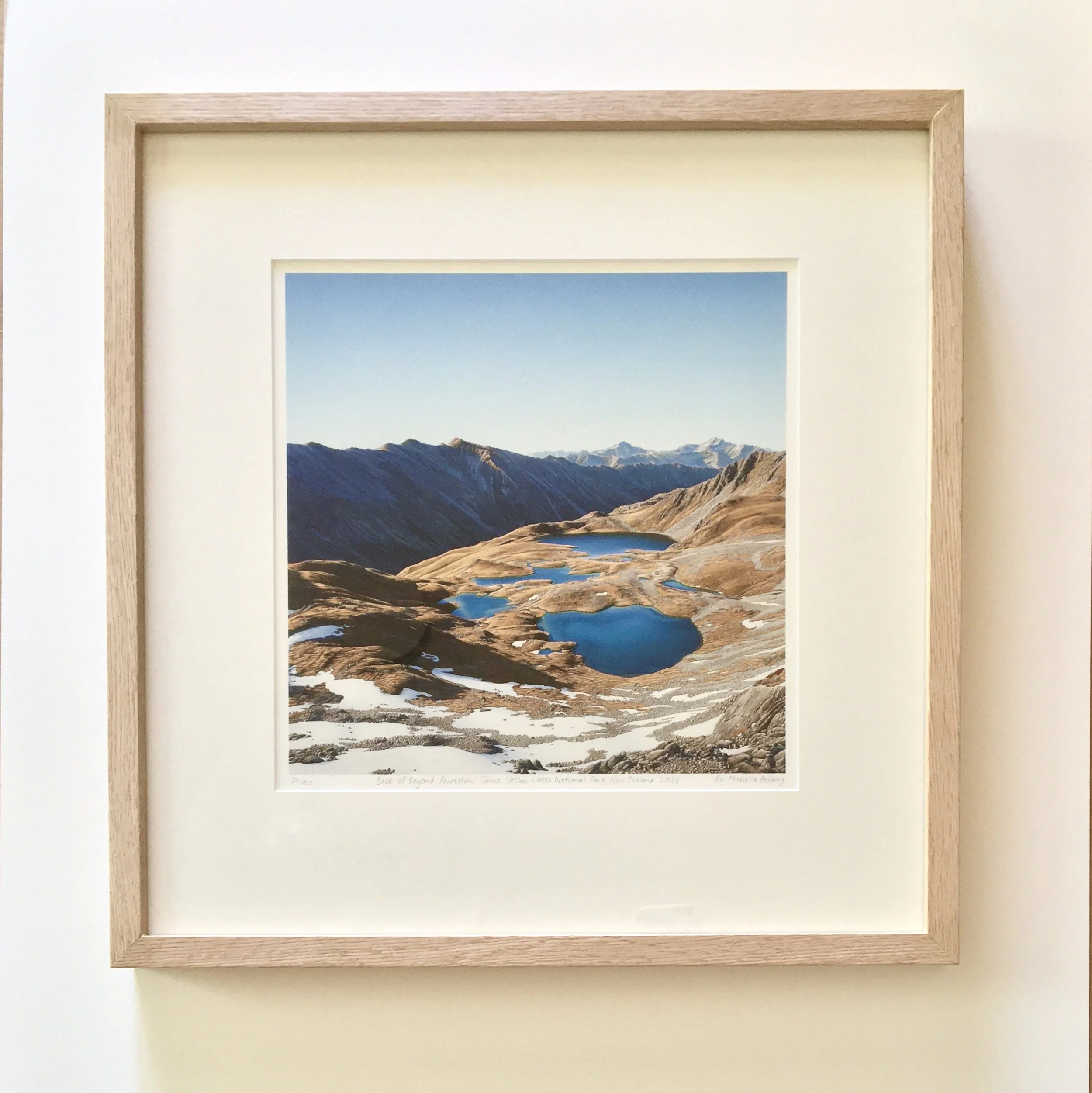 Framed painting of mountains and lakes with a light-colored wooden frame by realist painter Michelle Bellamy. 