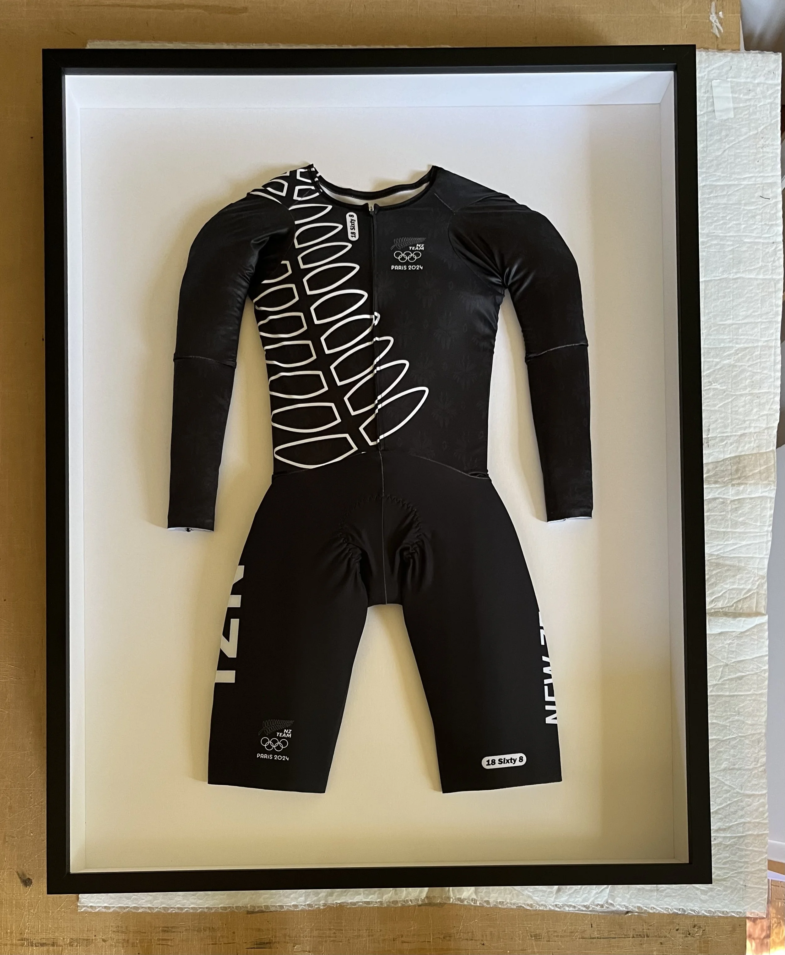 A framed cycling jersey with black and white design, featuring logos for the 2024 Paris Olympics, New Zealand team's logo, and the name '18 Slyty 8' at the bottom right.