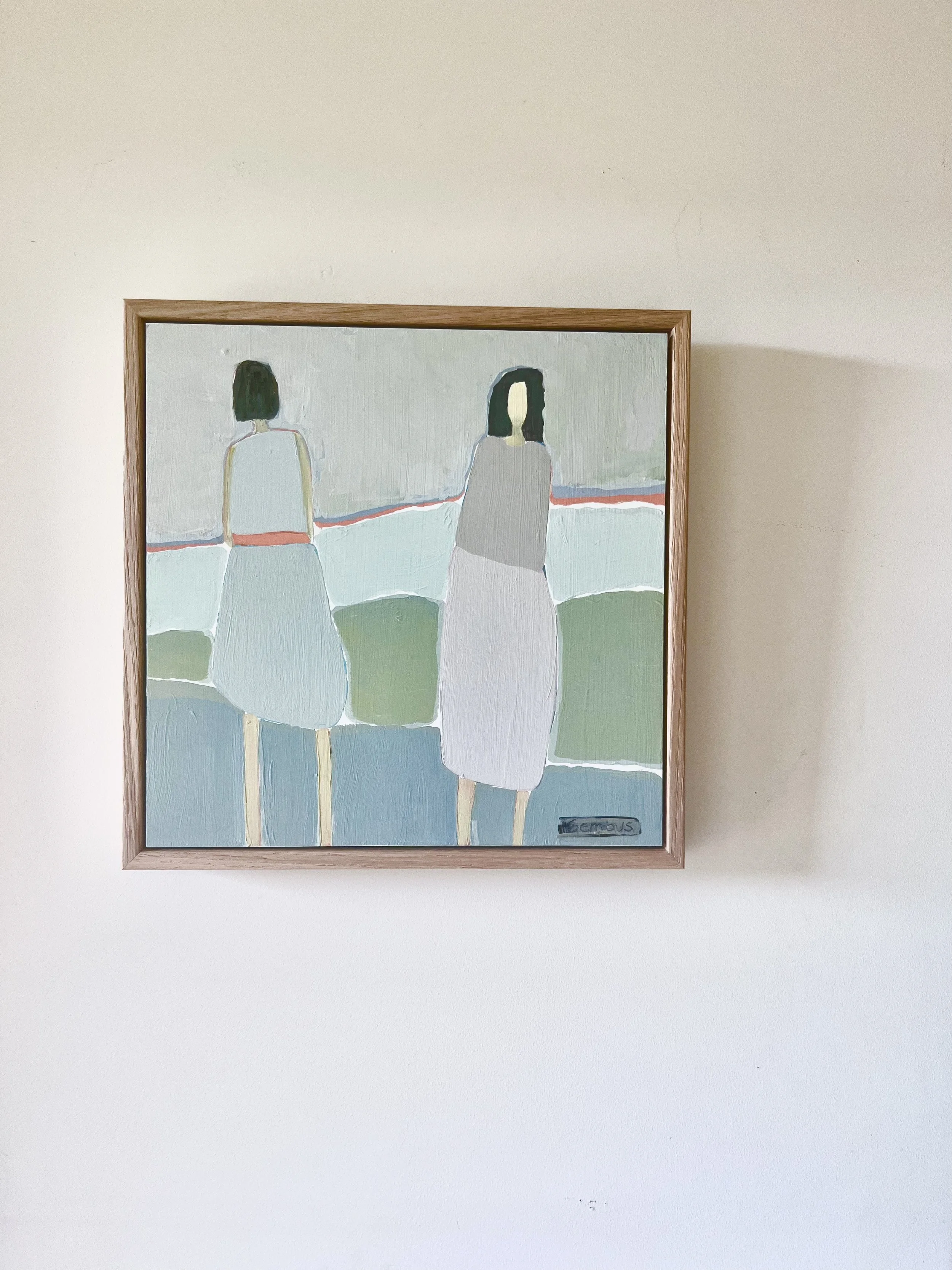 A framed painting depicts two women sitting on a bench, facing away, with a simple background. The woman on the left has short dark hair and wears a sleeveless top and a skirt, while the woman on the right has long dark hair and wears a long dress. T