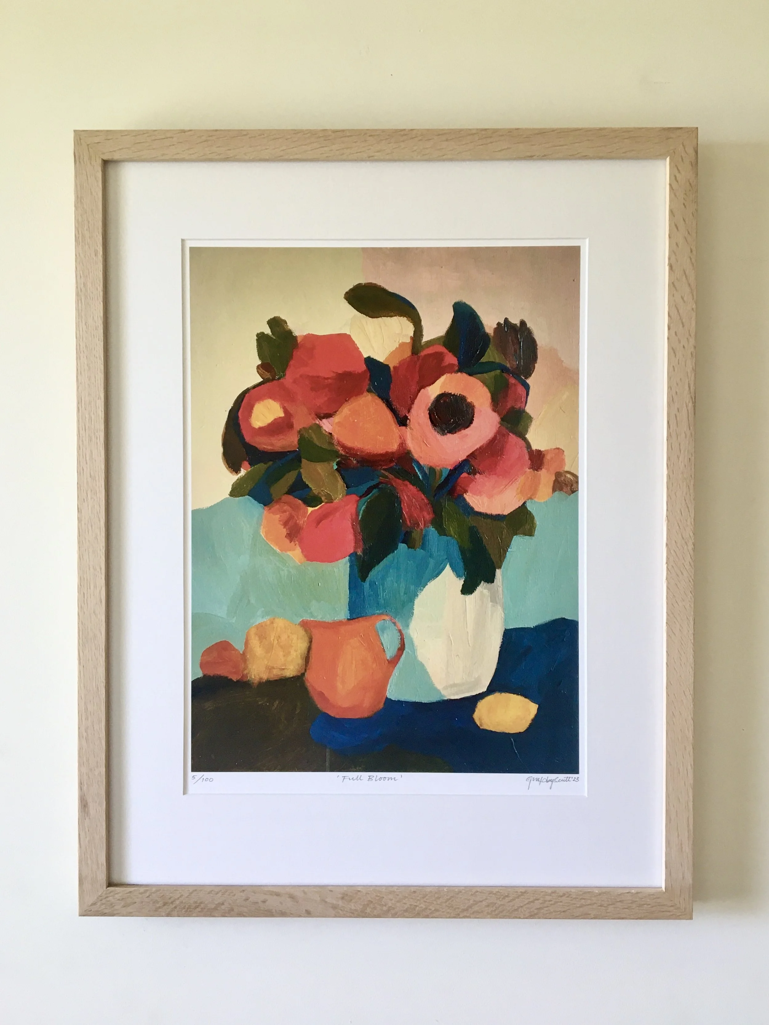 Framed painting titled 'Full Bloom' by New Zealand artist Georgina Hoby Scutt.
Depicts a colorful bouquet of flowers in a white vase on a dark surface, with a yellow flower at the bottom.