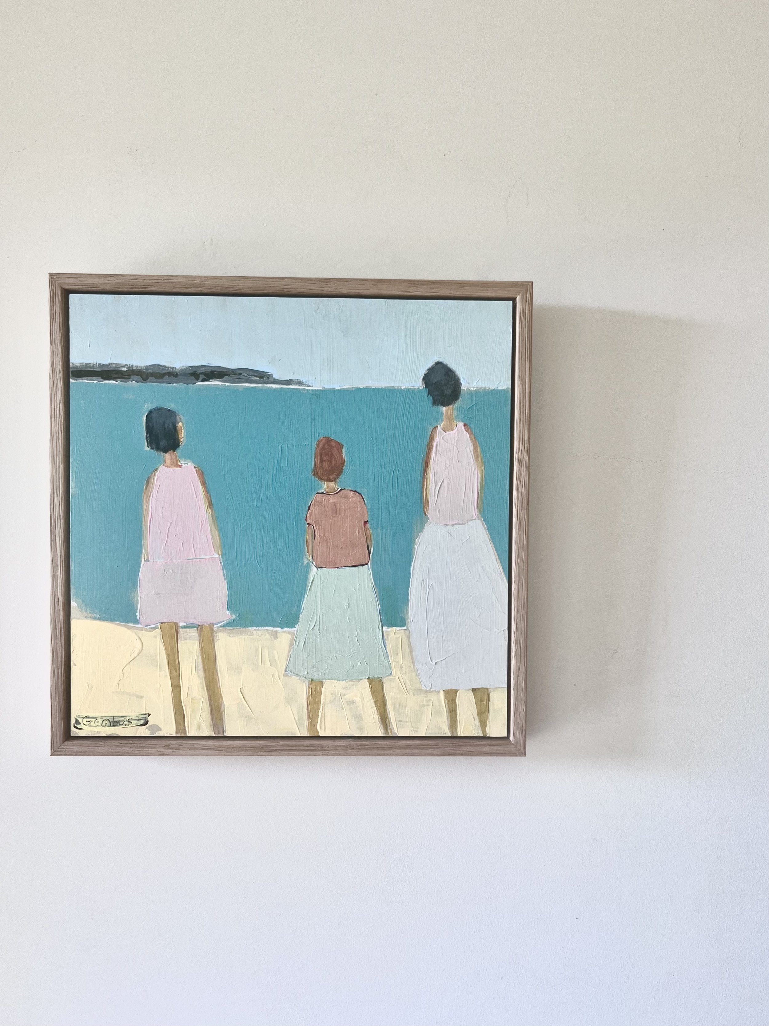 A painting of three women standing on a beach facing the water, wearing dresses in pastel colors, with a distant shoreline under a cloudy sky. The artist is Karin Gembus.