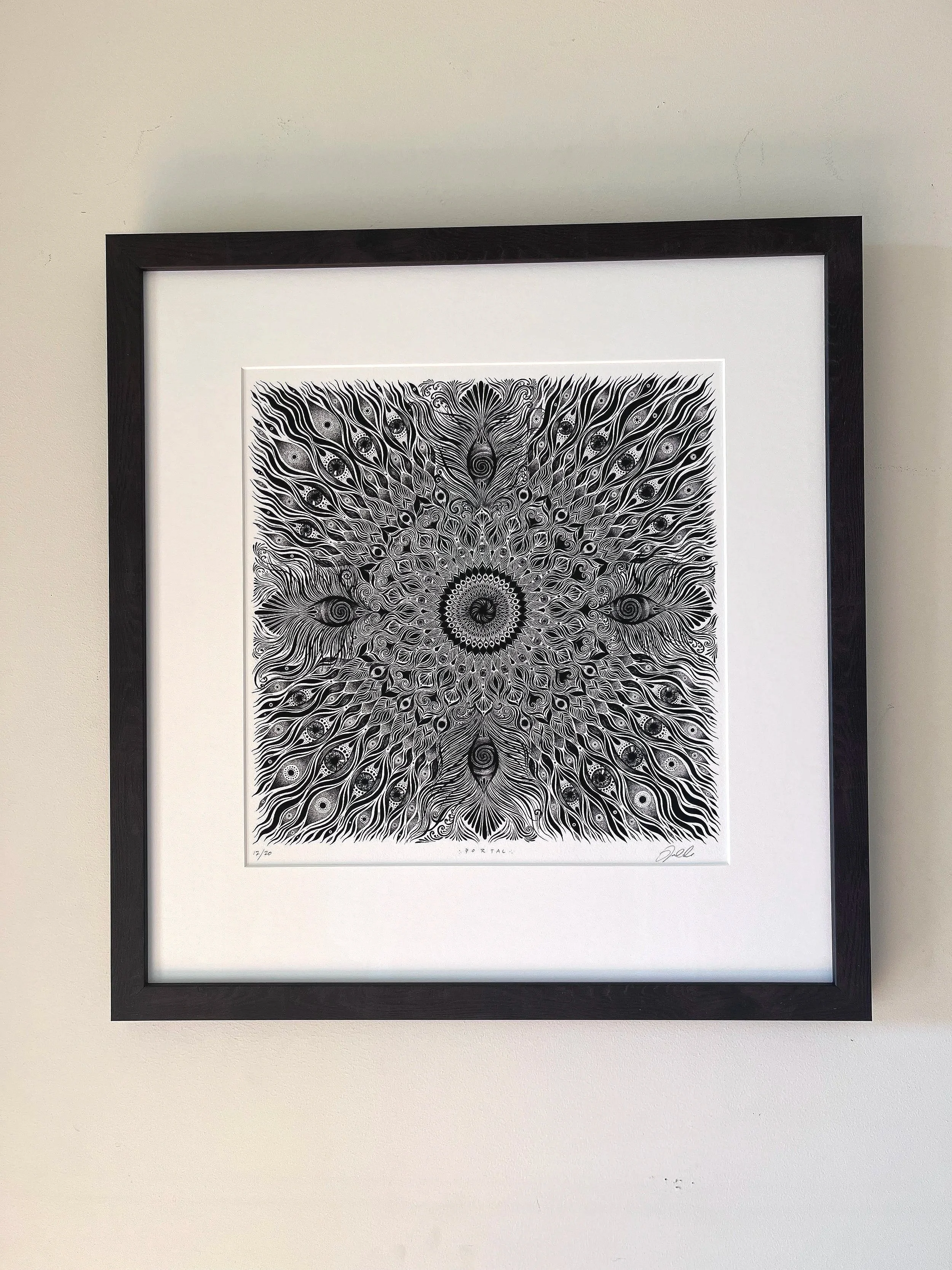 Black-and-white abstract peacock feather mandala artwork framed on a wall.