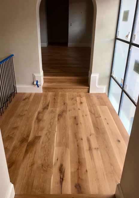 Wooden floor in a hallway with an arched doorway leading to another room, and a large window with frosted glass on the right.