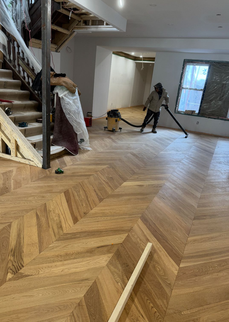 Worker installing or finishing a patterned hardwood floor in a house under renovation.
