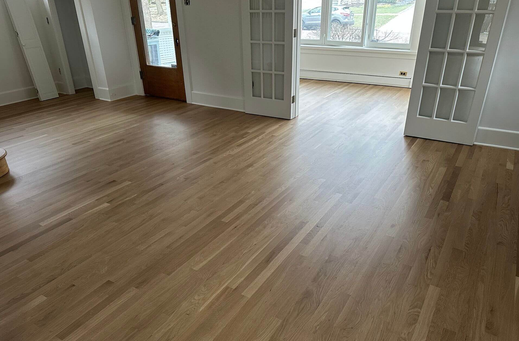 Empty room with light-colored hardwood floors, large windows, and open double doors with glass panels.