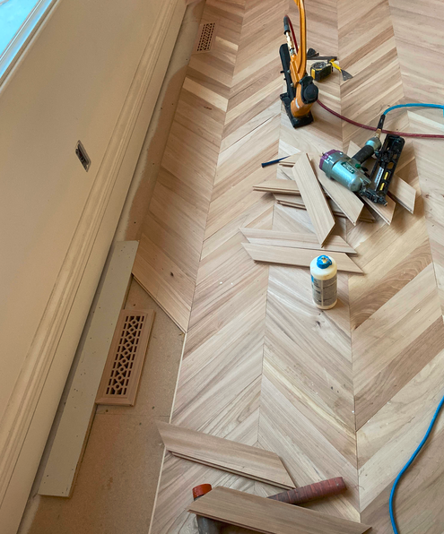 Flooring installation tools and wood pieces on a wooden floor, with a level, glue, and a nail gun visible.
