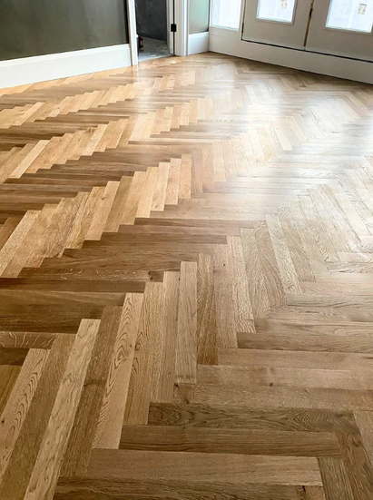 Photo of a herringbone hardwood floor inside a room with a door and windows.