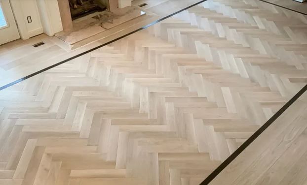 Finished light wood parquet flooring in a herringbone pattern in a room under construction.