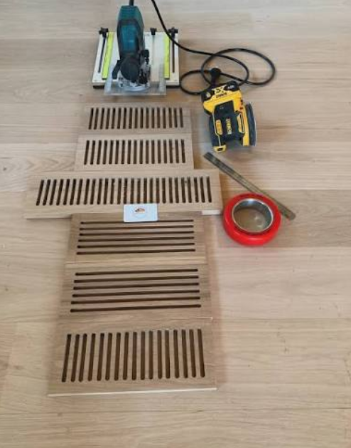 Power saw, measuring tape, and six wooden vent covers on a wooden floor.