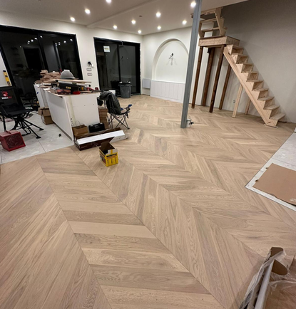 Interior view of a room under renovation with new light wood flooring, a staircase, and unfinished furniture and tools.