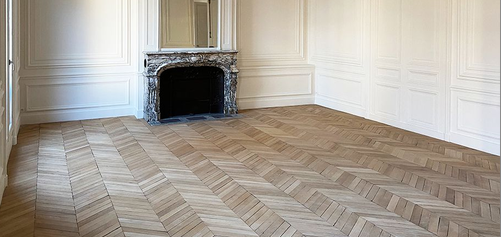 Empty room with wood herringbone floor and a fireplace with marble mantel.