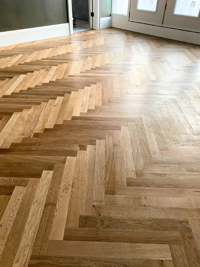 Close-up of a hardwood floor with a herringbone pattern near a glass door.
