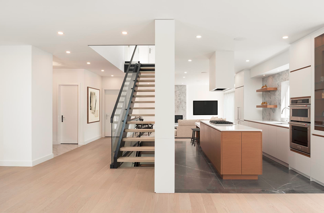 Open-concept modern living space with a kitchen and staircase, featuring white walls, wooden accents, and sleek appliances.