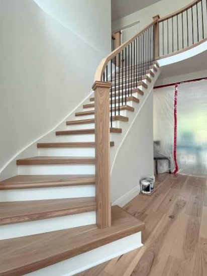 Curved wooden staircase inside a house with light-colored steps and a wooden railing.