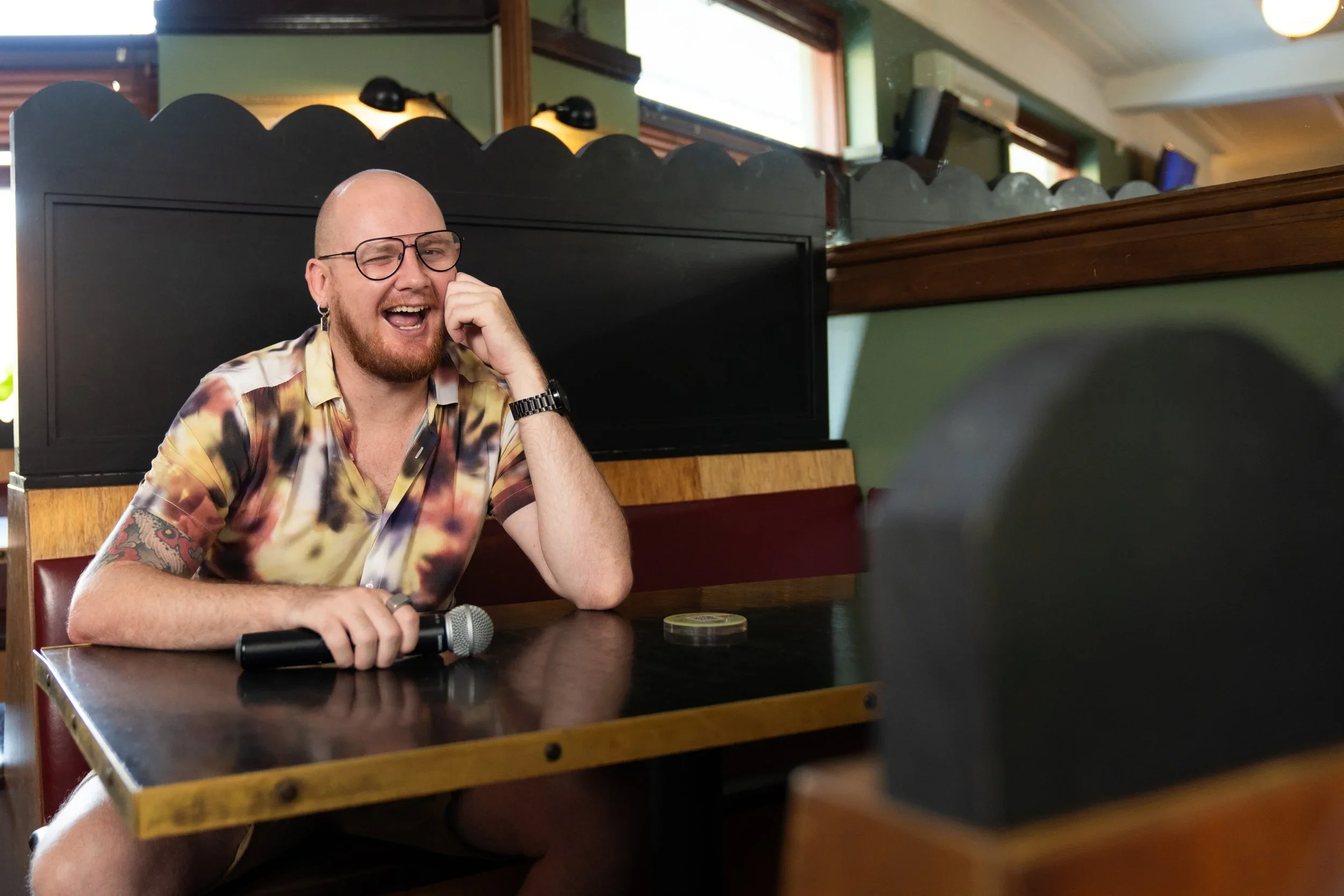 Four friends sit around a table at a restaurant, enjoying drinks and conversation. They are smiling and engaging with each other, with food and drinks on the table.