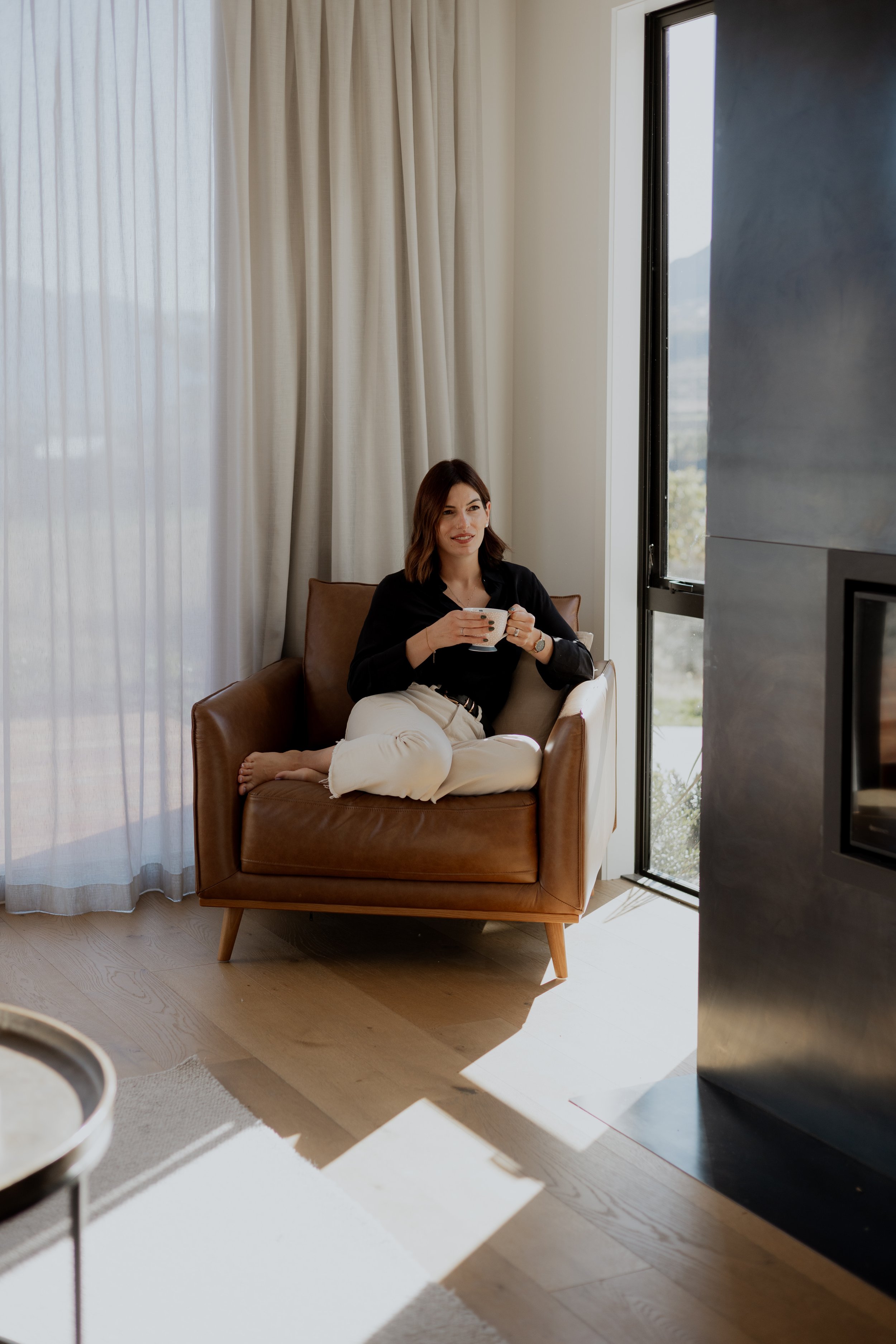 Courtney, designer and creative at Kindred by Courtney - sitting in her chair sipping tea in her home in Queenstown.