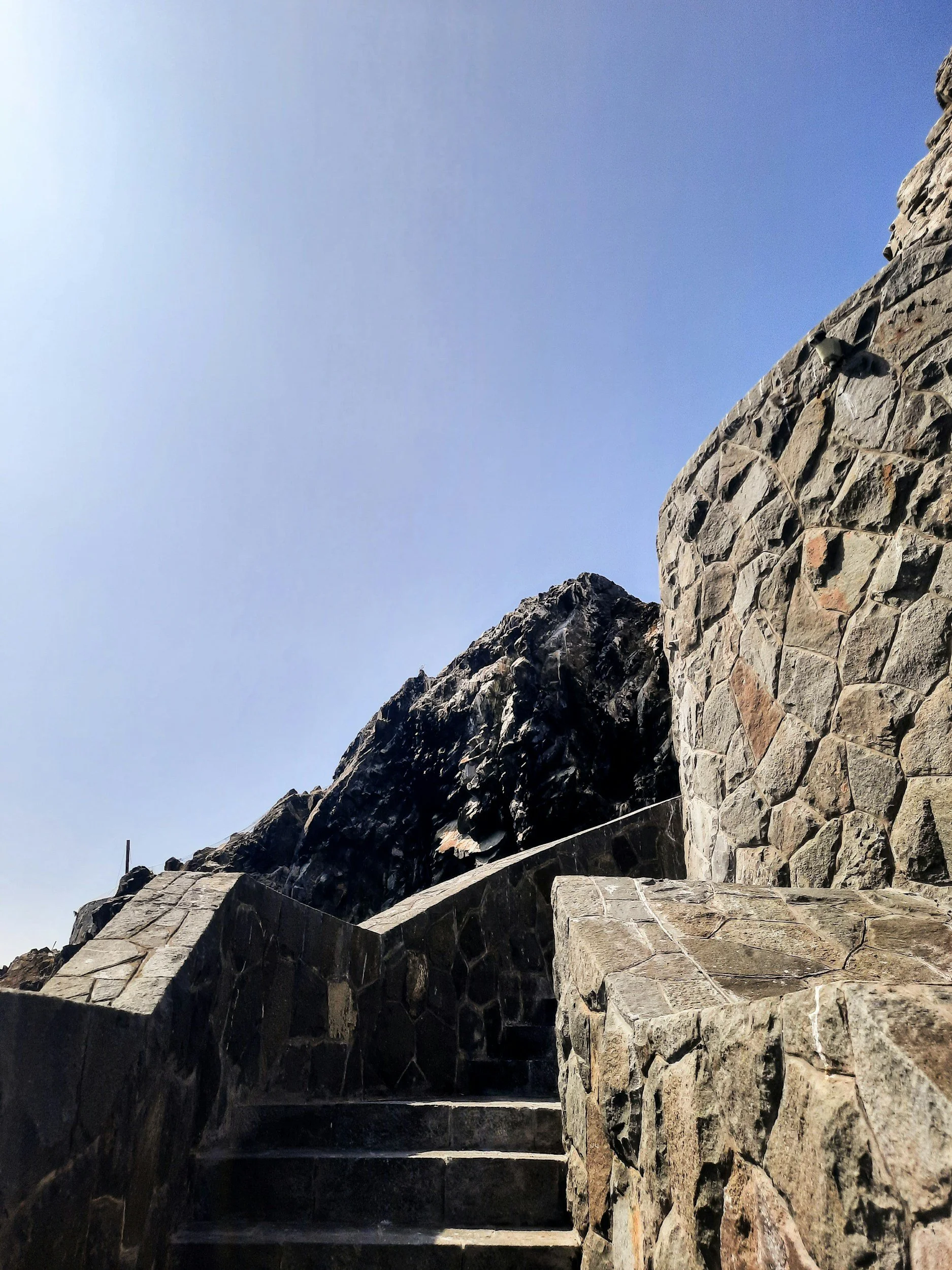 Stone steps leading up to a castle or fortress wall built from large, rough-cut stones, with a clear blue sky in the background.