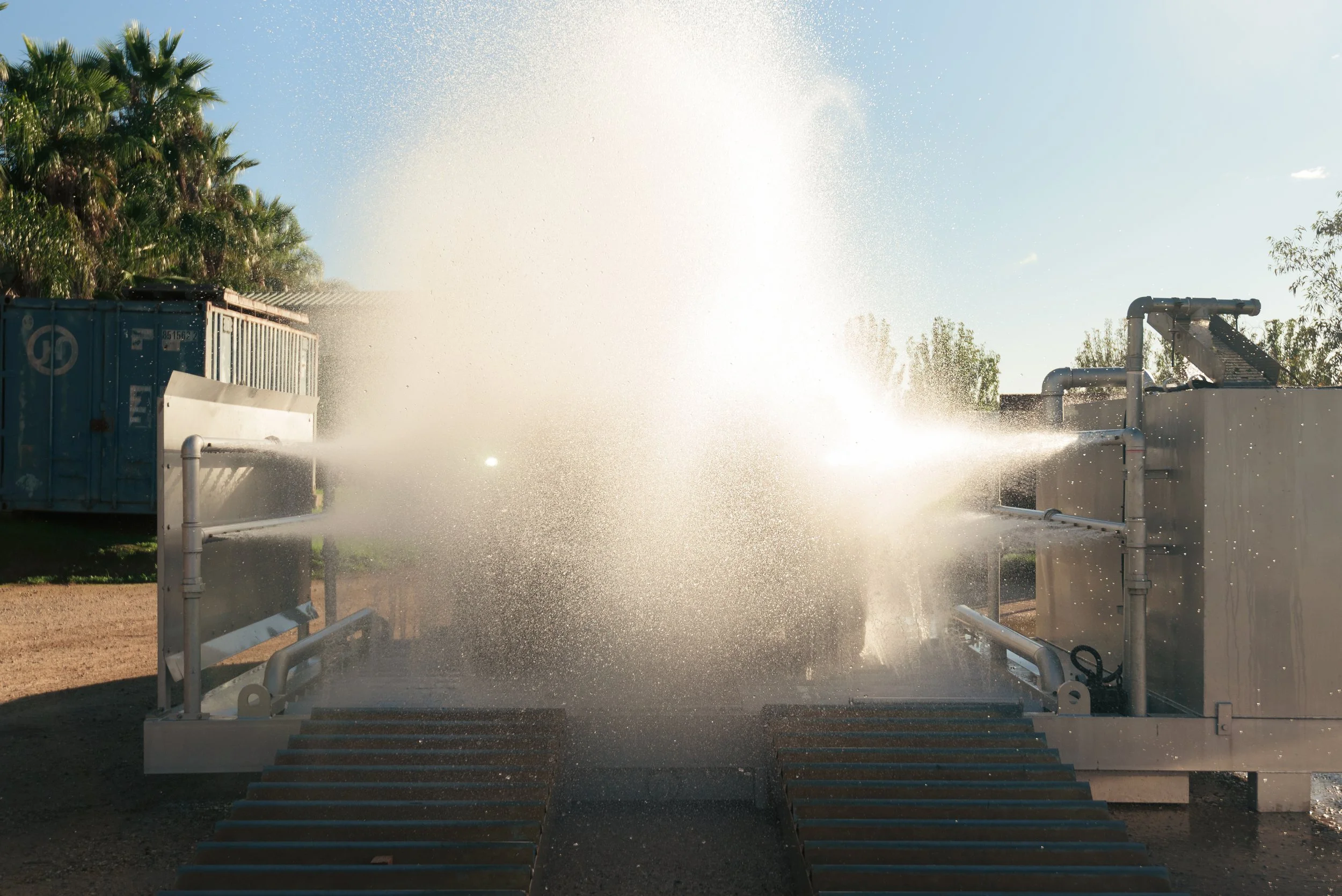 Water spray from industrial equipment creates a mist in the air, with trees and blue sky visible in the background.