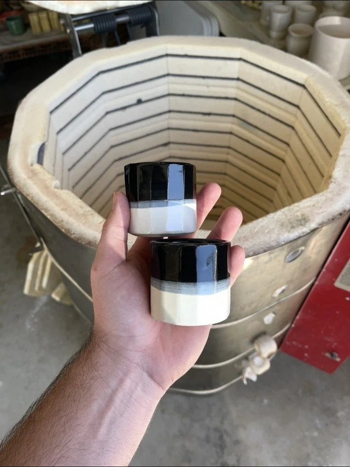 Two finished glazed cups held in front of John's open kiln
