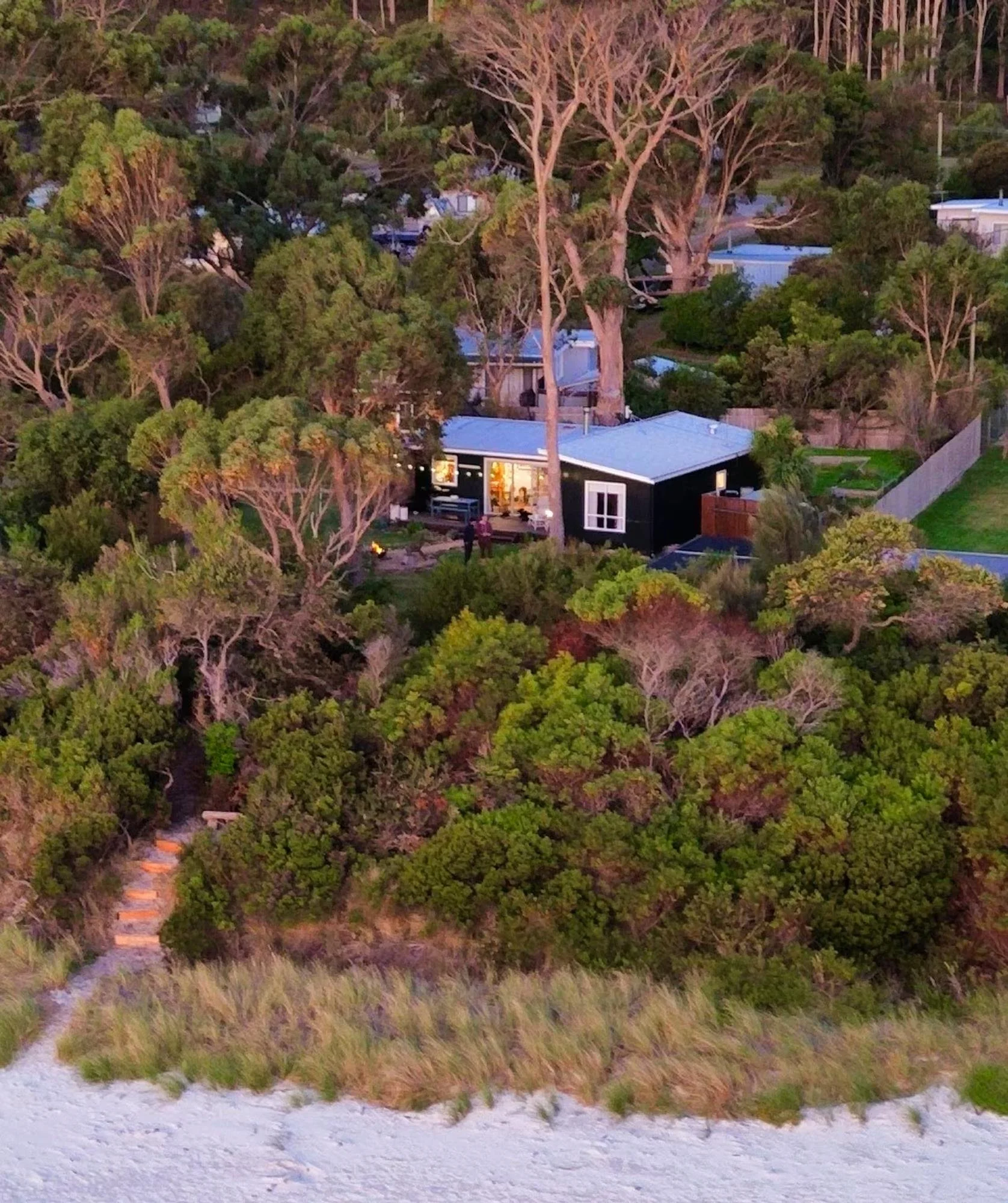 A landscape scene with trees and houses, seen from a low, uneven gravel path in the foreground during dusk.