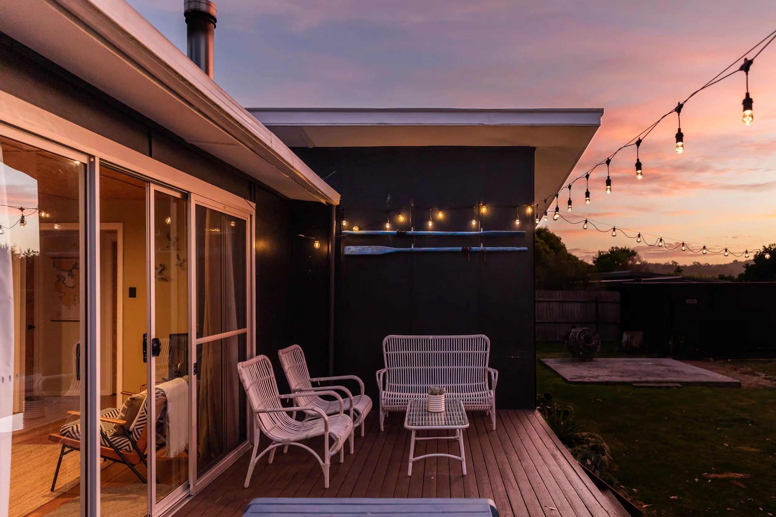 Outdoor deck at sunset with string lights, white chairs and a pink sky