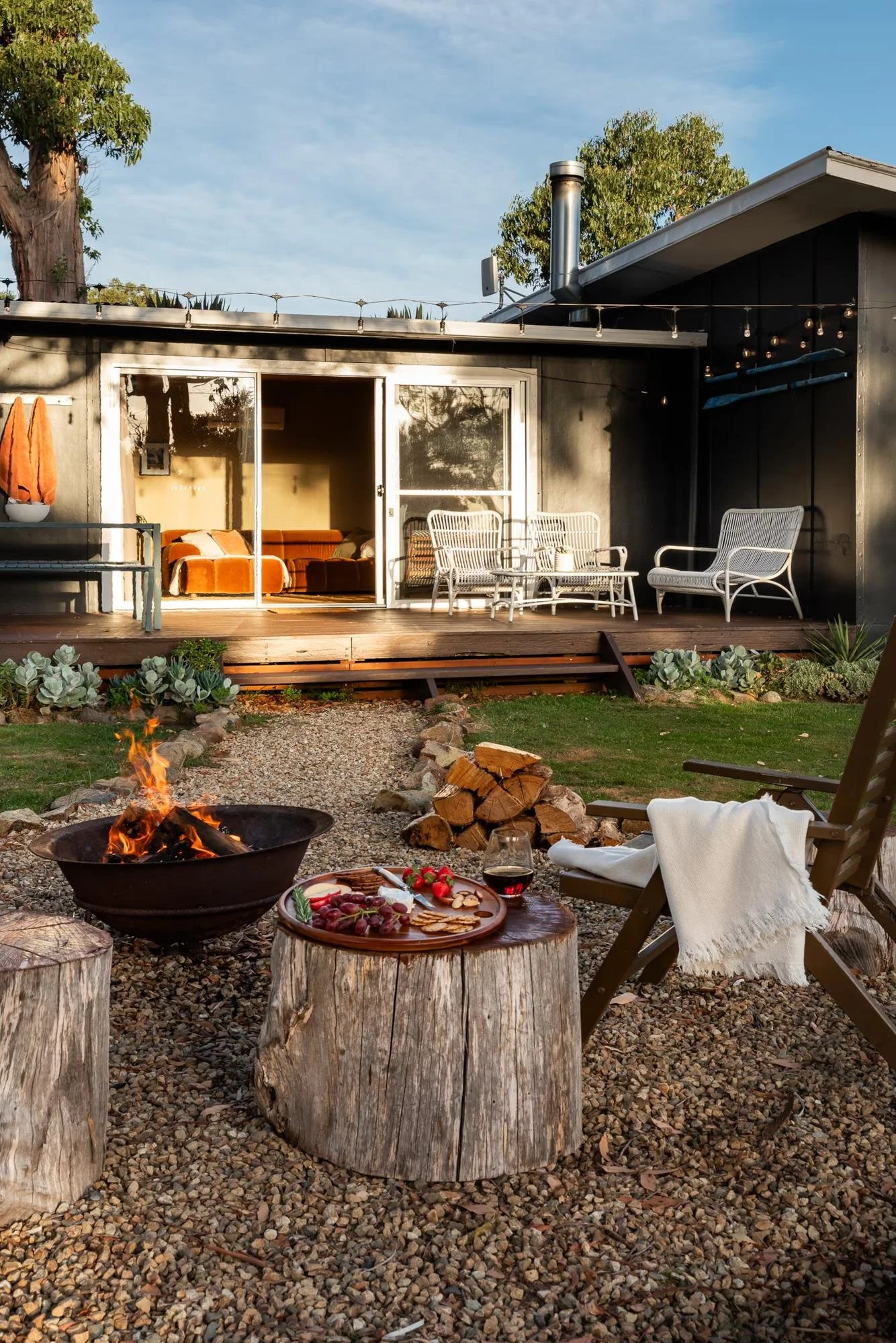Outdoor seating by the fire pit with snacks, red wine and string lights