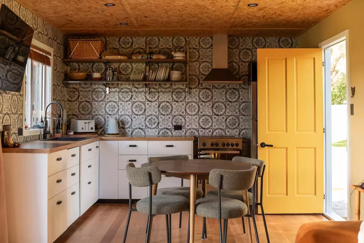 Retro kitchen with patterned tiles, open shelving, a yellow door and a round dining table