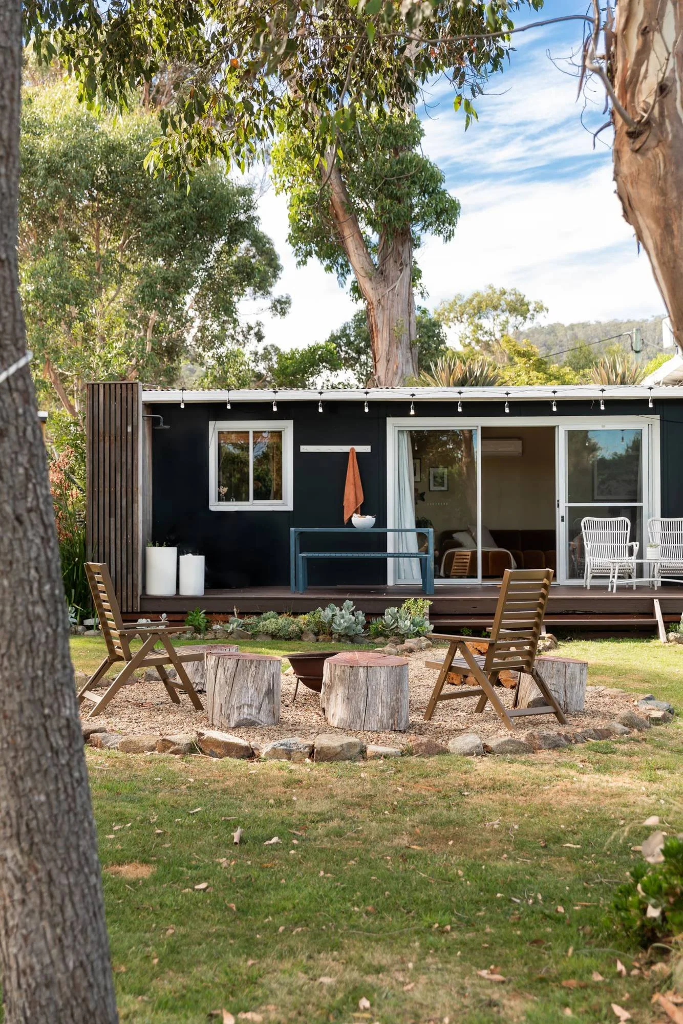 Grassy backyard with outdoor chairs, timber stools and string lights