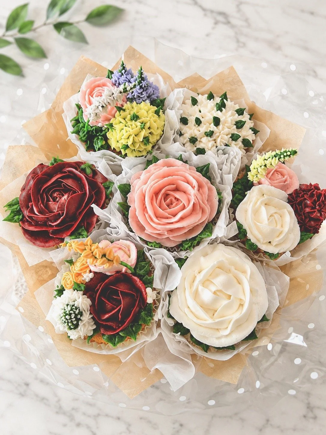 Colorful cupcakes decorated to look like roses and flowers, arranged in a bouquet style on a marble surface.