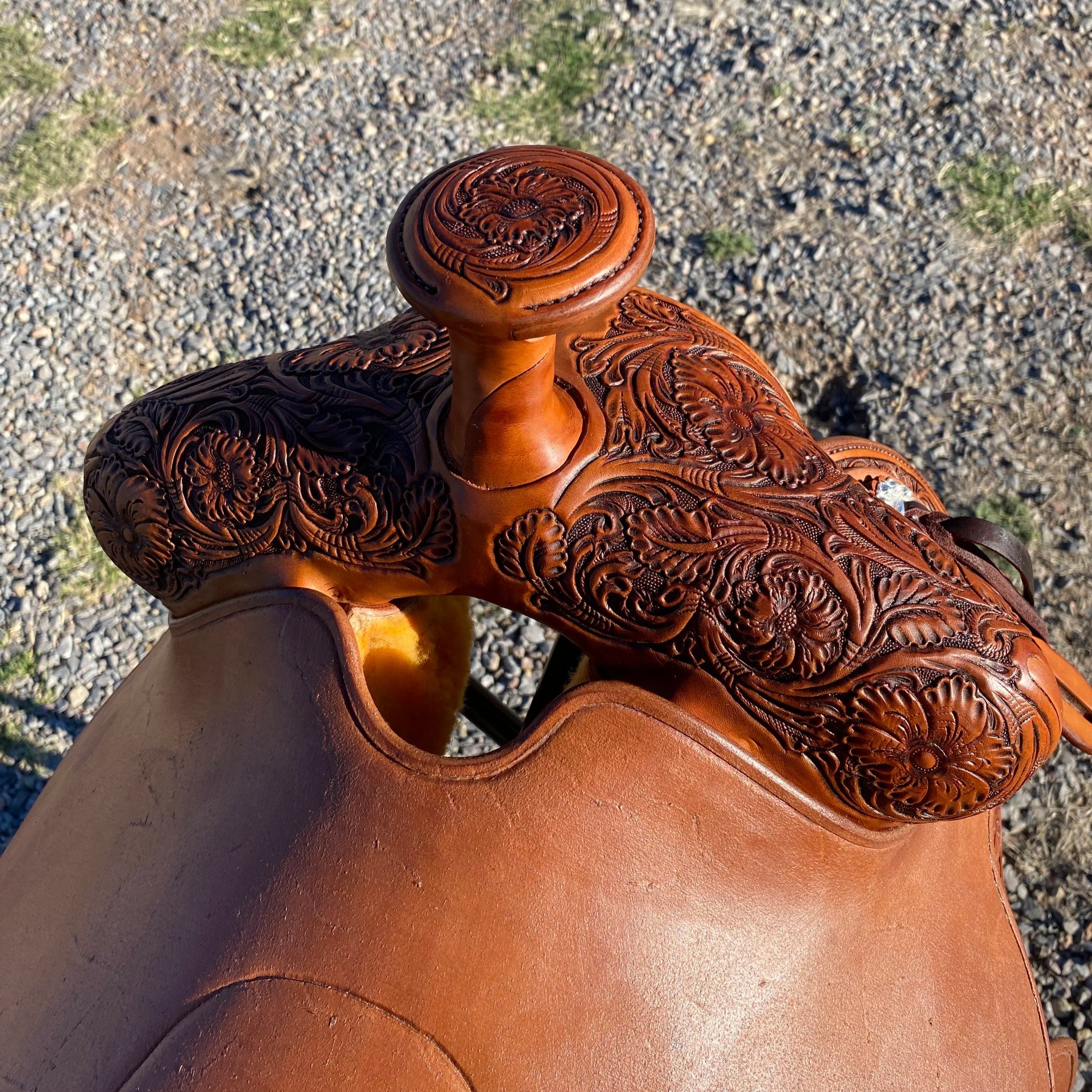 A wooden sculpture of a dragon with intricate carvings, held by a person's hand. The background shows gravel and a patch of grass.