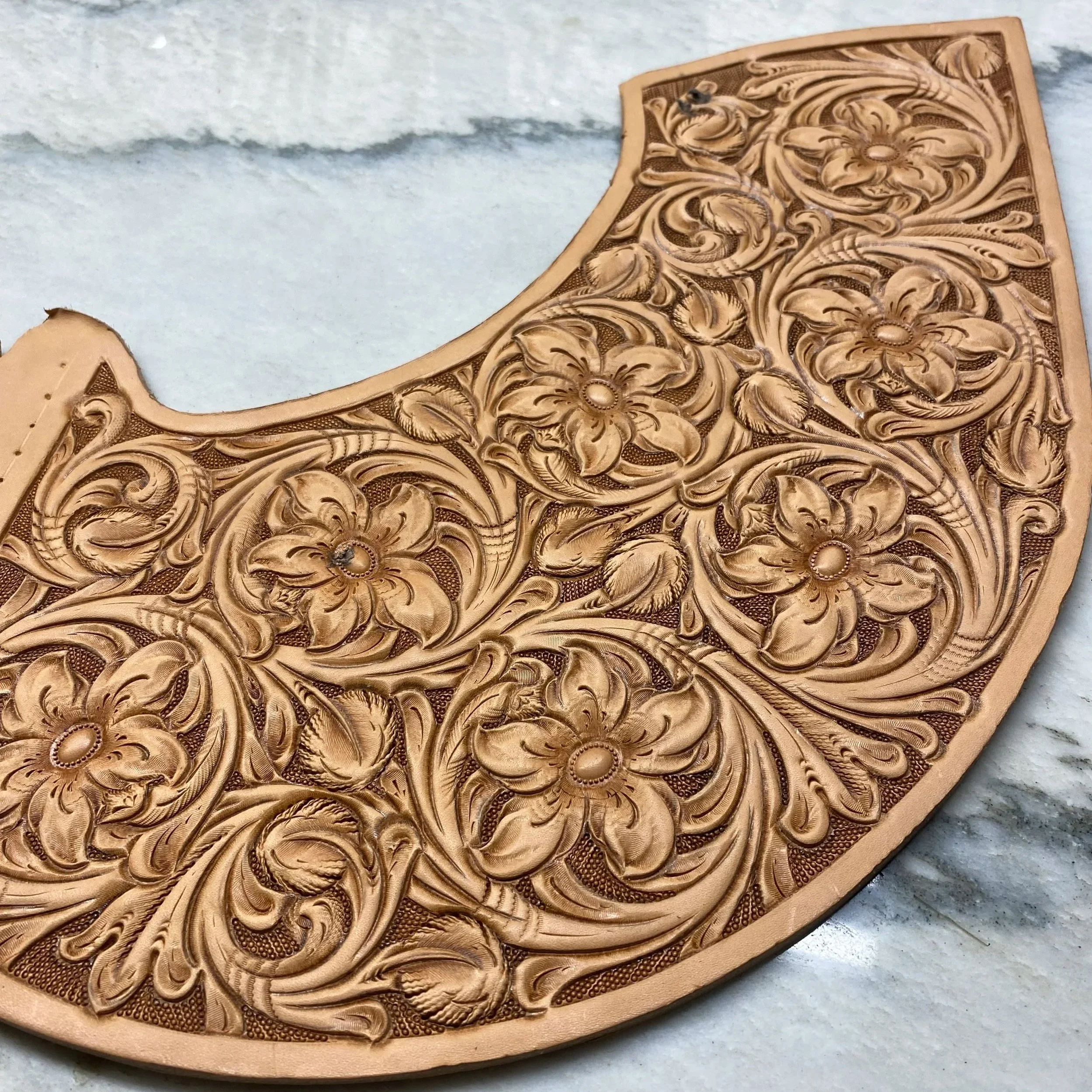 A close-up of an intricately carved wooden piece with floral and swirling patterns on a light-colored surface.