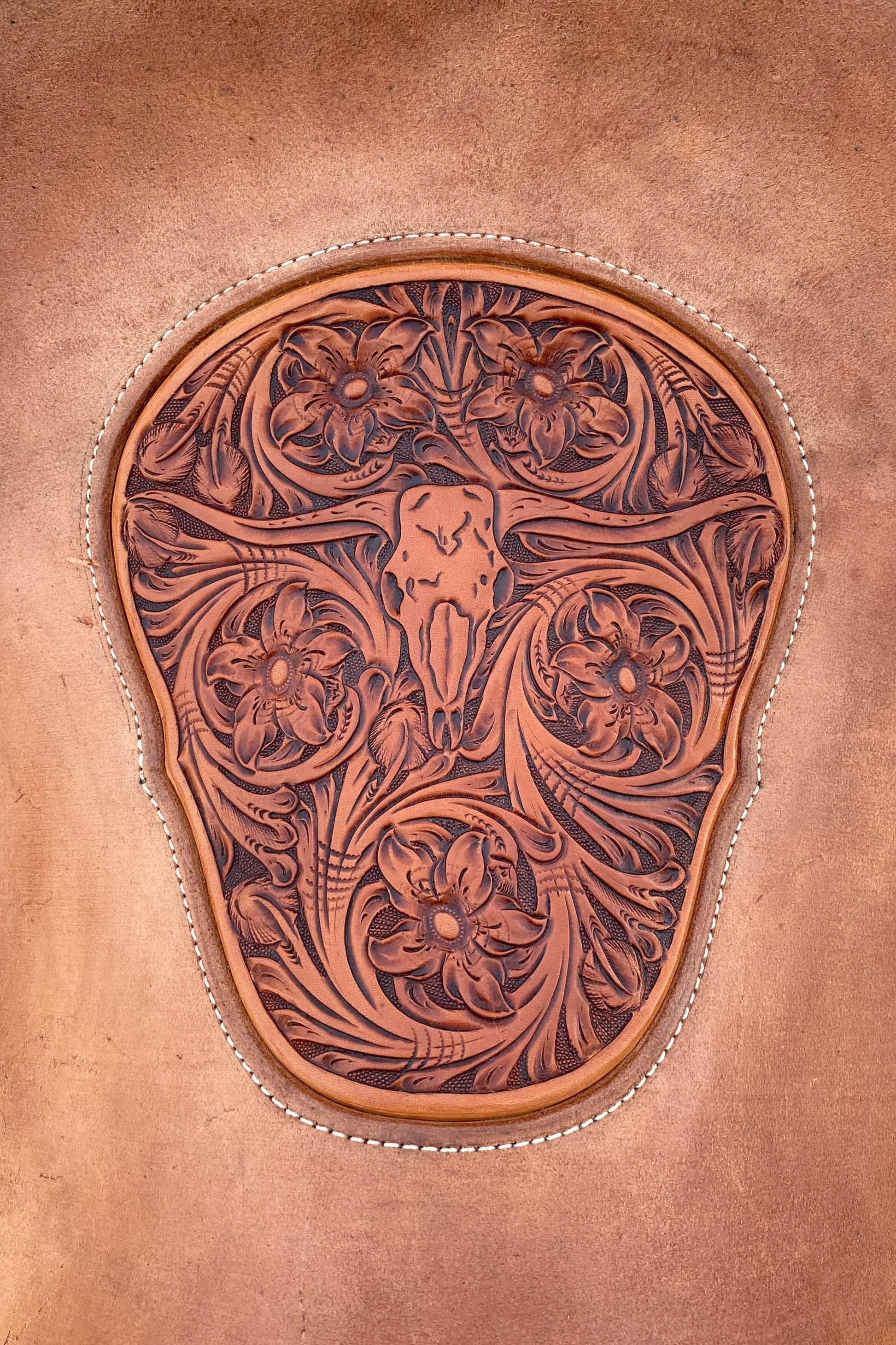 Close-up of a carved leather saddle with floral patterns against a tan leather background.