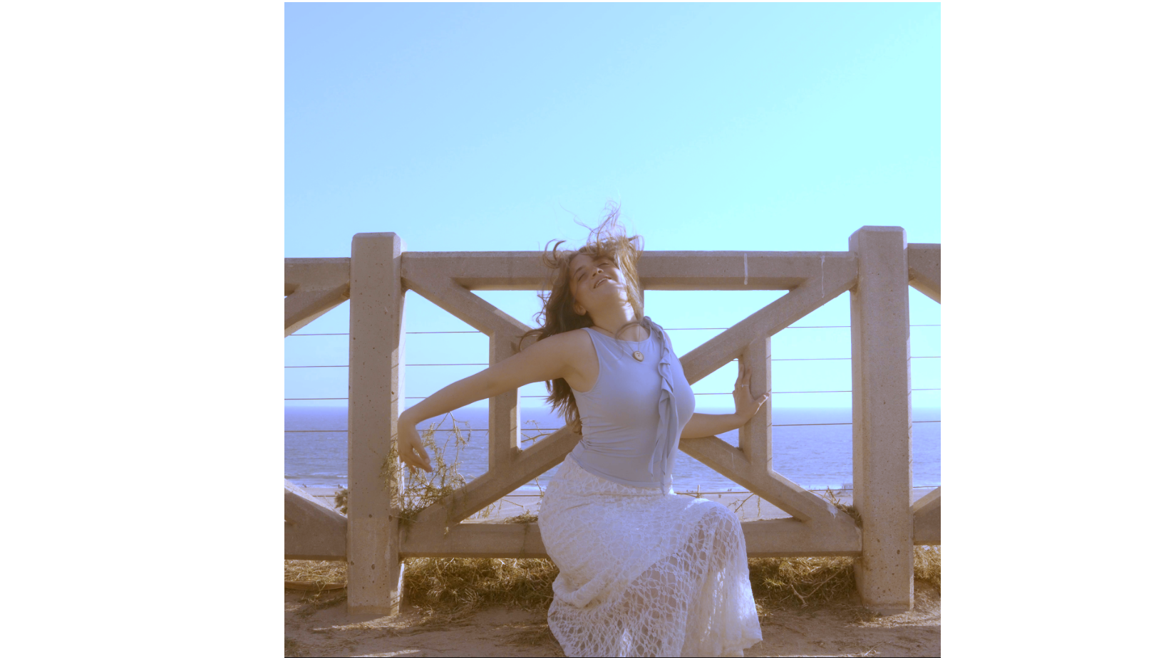 Natalia James standing beside a wooden railing overlooking the ocean.