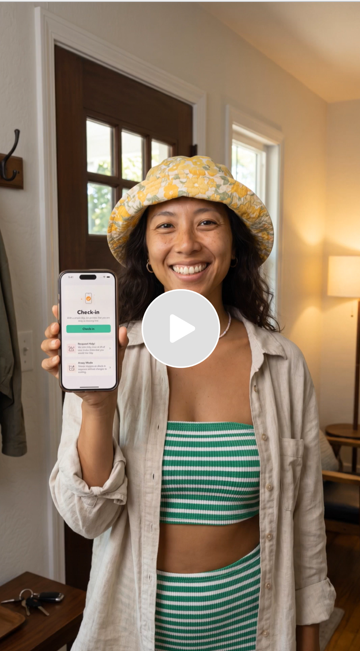 Smiling woman wearing a yellow floral hat holding up a smartphone showing a check-in confirmation in a well-lit room.