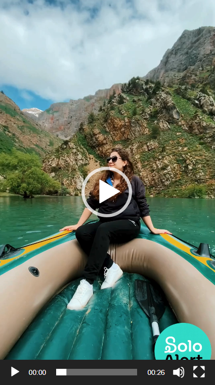 A woman with sunglasses and dark clothing sitting on an inflatable boat in a river surrounded by mountainous terrain with green vegetation and rocky cliffs.