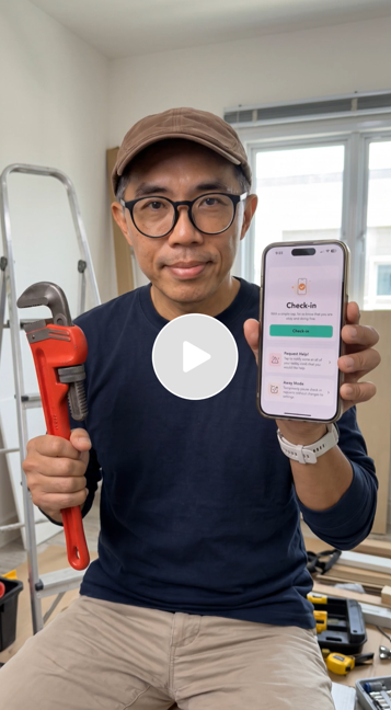 Man wearing glasses and a brown cap holding a large red pipe wrench in his right hand and a smartphone in his left, displaying a check-in app, in a room with a ladder and window in the background.