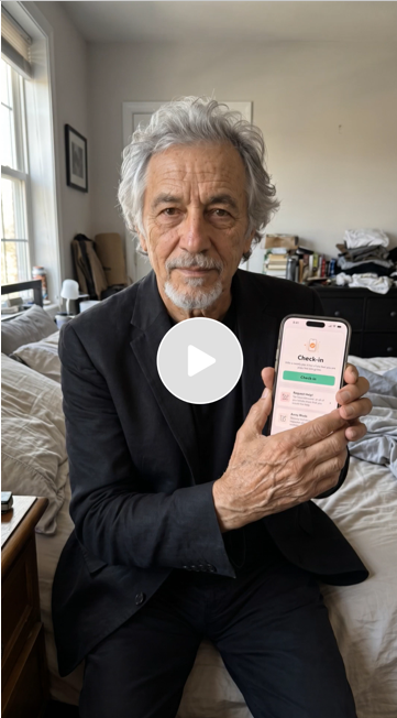 An older man with gray hair and a beard sitting on a bed in a bedroom, holding a smartphone displaying a check-in app.