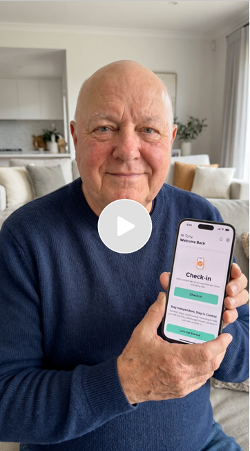 An elderly man holding a smartphone displaying a check-in screen, sitting in a bright living room.