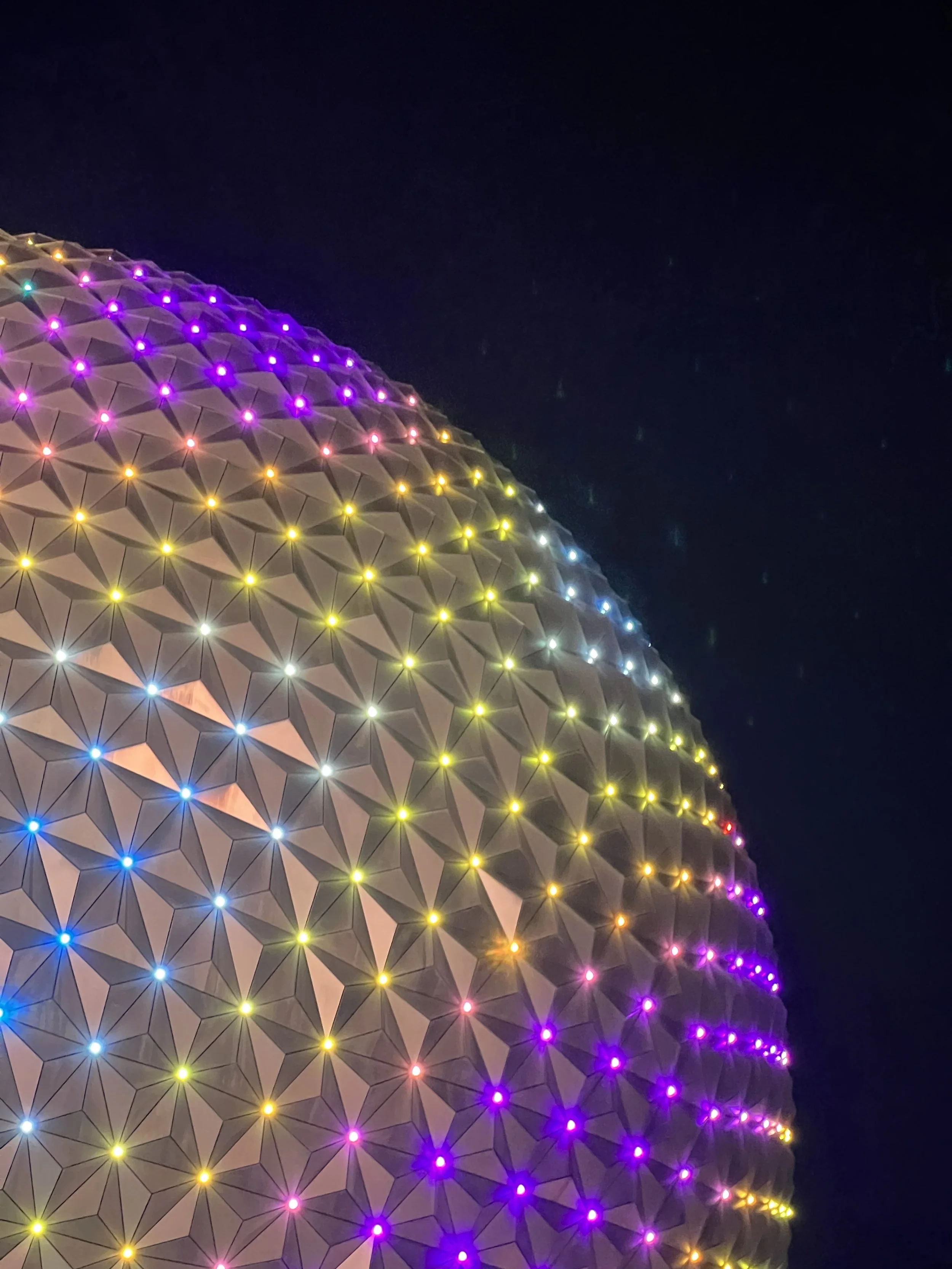 Close-up of the Illuminations of Spaceship Earth statue at EPCOT theme park, decorated with colorful lights at night.