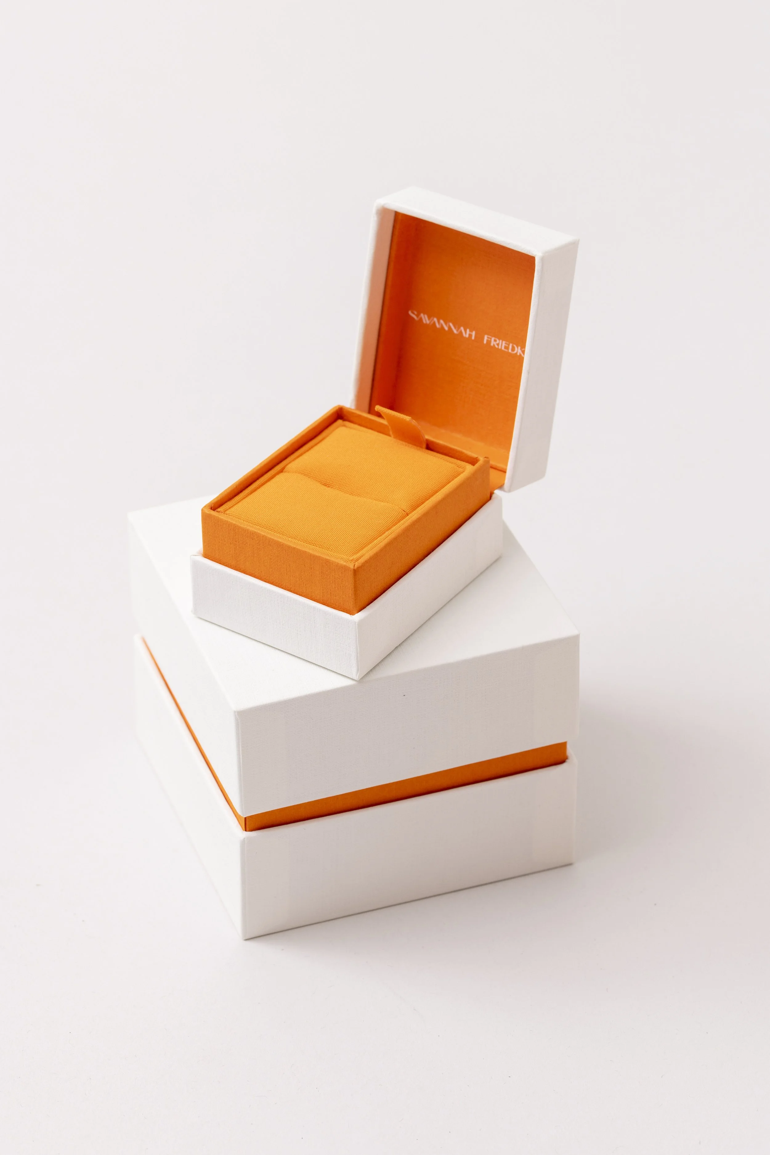 An open white box with orange interior, a cushion inside, placed on a white surface with another similar box underneath.