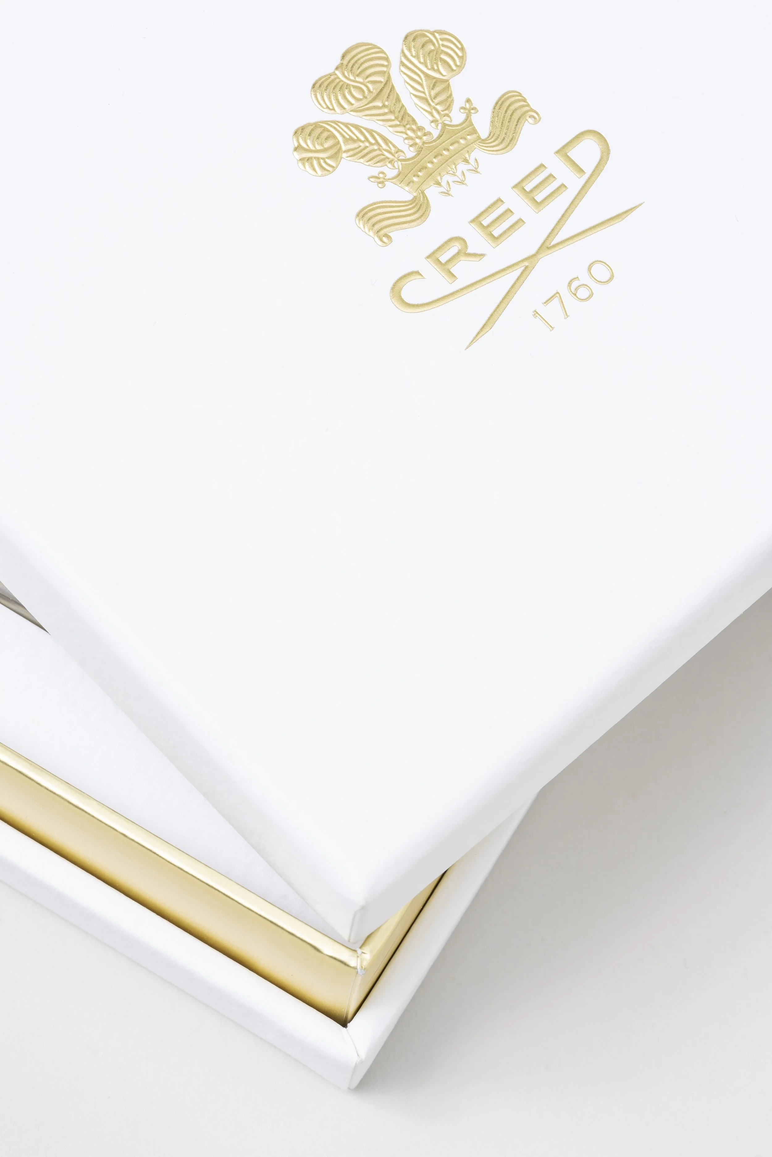 Close-up of a white gift box with a gold trim, featuring an embossed gold crest and the text 'CREED 1760'.