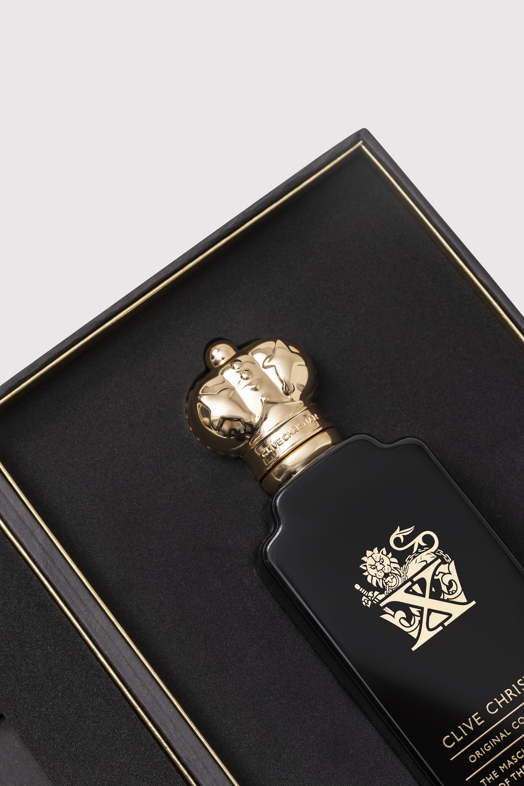 A black box containing a gold-tone bottle with a lion logo and a black label with gold text reading 'Clive Christian,' featuring a regal emblem, inside a box with gold trim.