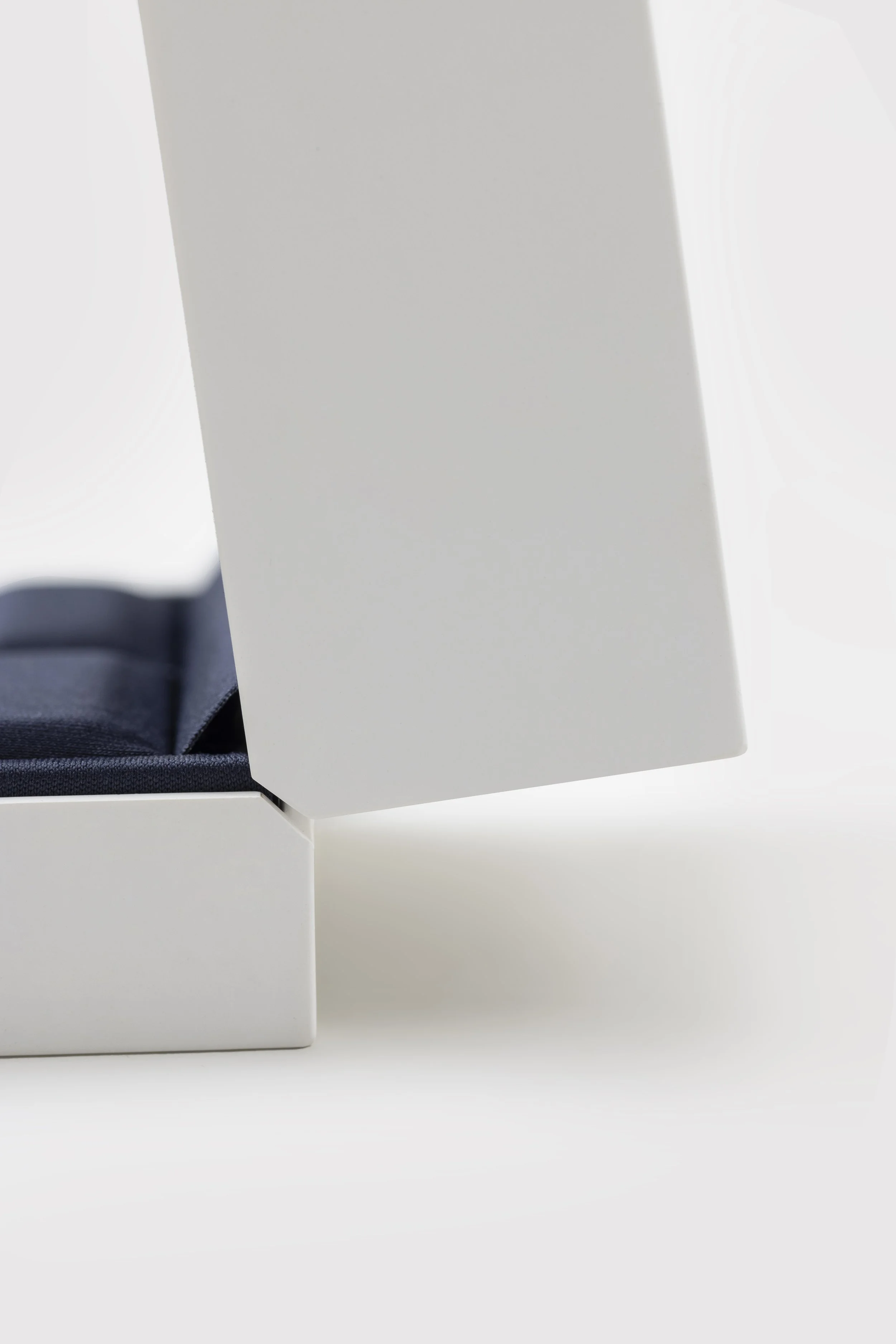 Close-up of a white box with a partially opened lid revealing a dark interior, placed on a plain light surface.